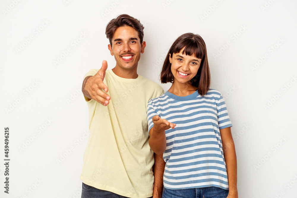 Fototapeta premium Young mixed race couple isolated on white background stretching hand at camera in greeting gesture.