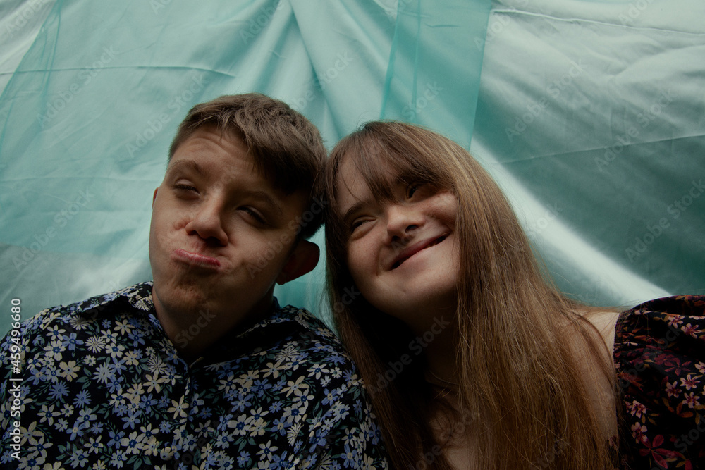 Portrait of young couple with Down Syndrome and Foetal Alcohol Syndrome being silly in front of blue background Portrait of young couple with Down Syndrome and Foetal Alcohol Syndrome being silly in front of blue background