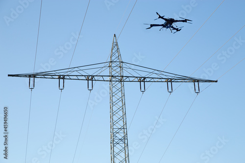 Drohne mit Kamera an Bord, die in einen Himmel fliegt, Strommast, Kabel und Isolatoren im Hintergrund