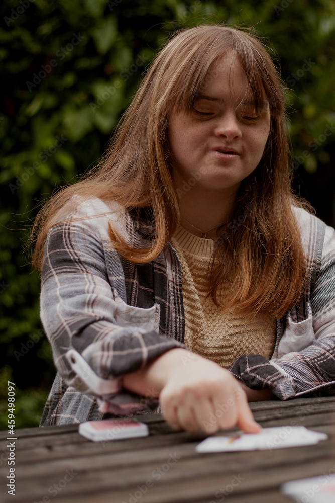 Young woman with Down Syndrome playing cards outdoors and looking confident Young woman with Down Syndrome playing cards outdoors and looking confident