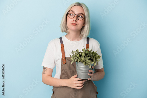 Young gardener caucasian woman holding a plant isolated on blue background dreaming of achieving goals and purposes