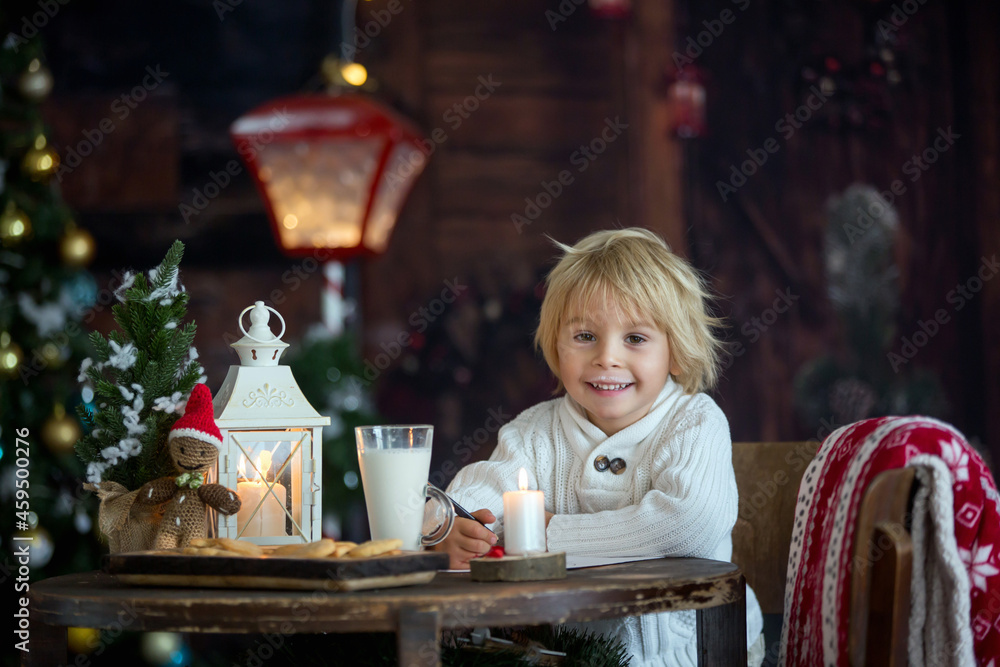 Beautiful toddler child, blond boy, writing letter to Santa Claus and eating cookies at home, cozy atmosphere Beautiful toddler child, blond boy, writing letter to Santa Claus and eating cookies at home, cozy atmosphere