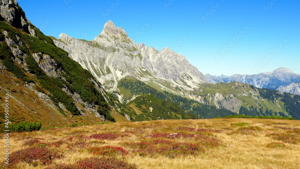 Gipfel der Zimba hinter herbstlich gefärbter Wiese, grünen Hängen und blauem Himmel im Vorarlberg