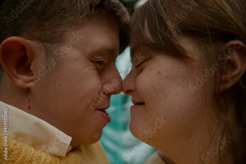 Face to face portrait of young couple with Down Syndrome and Foetal Alcohol Syndrome smiling and touching noses in front of blue background