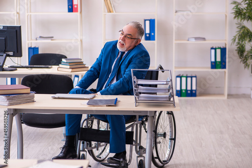 Old male employee in wheel-chair sitting in the office