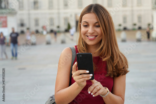 Hispanic young woman walking in the street paying online for e-commerce on her mobile phone