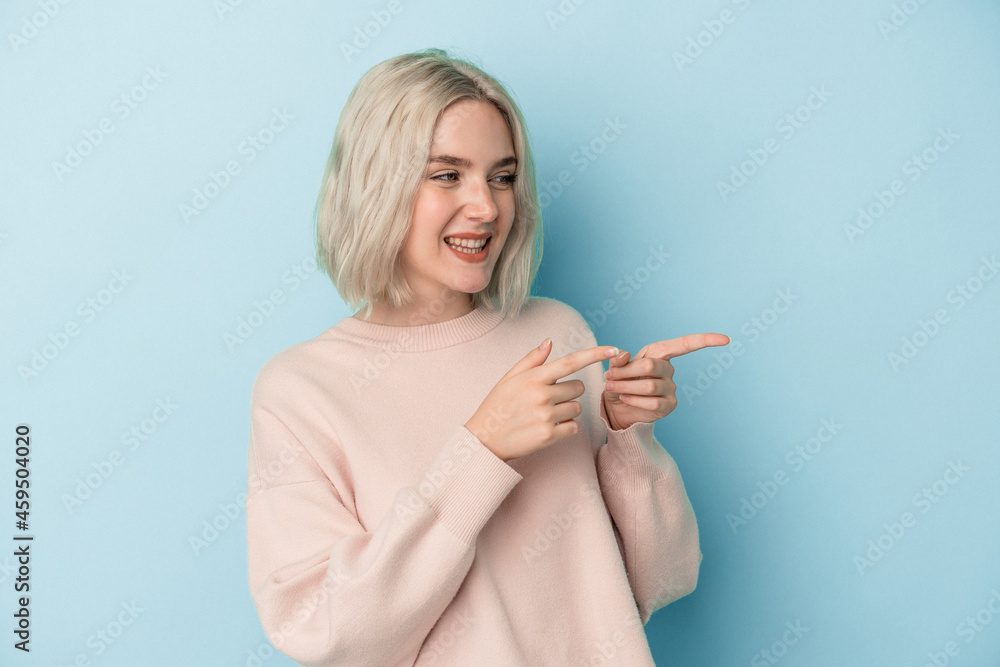 Young caucasian woman isolated on blue background points with thumb finger away, laughing and carefree. Young caucasian woman isolated on blue background points with thumb finger away, laughing and carefree.