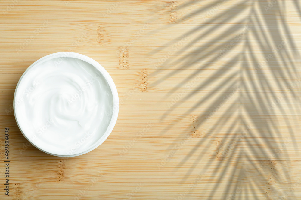 Cosmetic cream background. White cosmetic cream for skin and body in an open white jar on a wooden bamboo empty background. Cosmetic cream background. White cosmetic cream for skin and body in an open white jar on a wooden bamboo empty background.