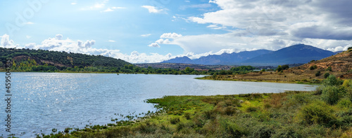 Panoramic mountain landscape with large sunny lake and small town on the shore.