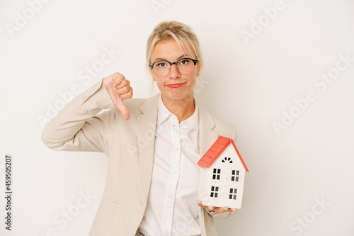 Young real estate agent woman holding a home model isolated on white background showing a dislike gesture, thumbs down. Disagreement concept.