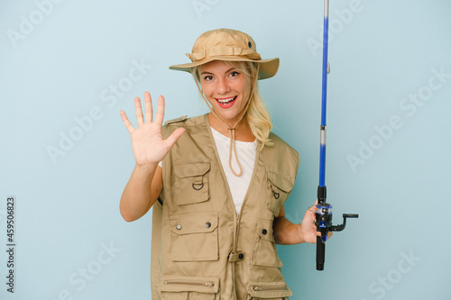 Young Russian fisherwoman isolated on blue background smiling cheerful showing number five with fingers.