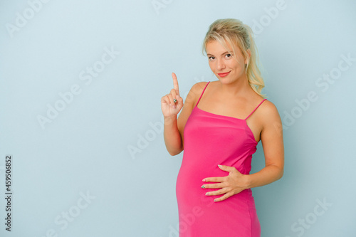 Young Russian woman pregnant isolated on blue background showing number one with finger.