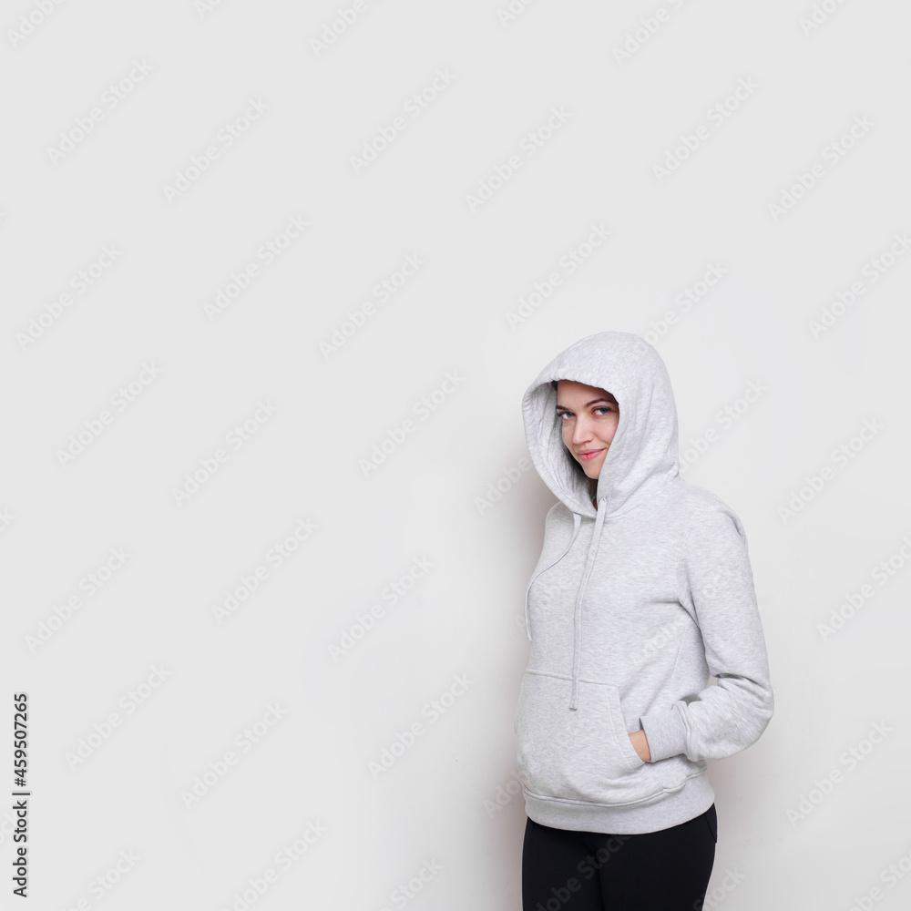 Cherful brunette girl dressed in a light grey sweater with hood on her head, isolated on white background. Copy space. Cherful brunette girl dressed in a light grey sweater with hood on her head, isolated on white background. Copy space.