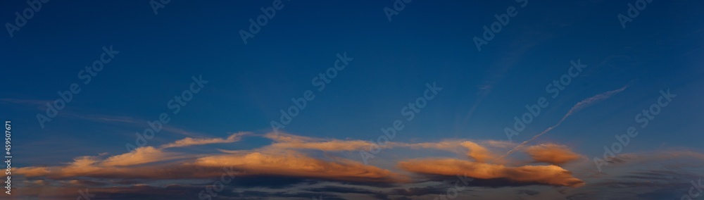Panorama of clouds illuminated by the setting evening sun
