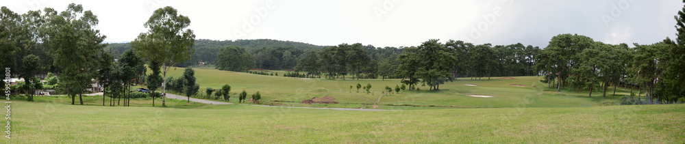 Panorama view of a landscape, golf club, park for visitors, trees, road, and cloudy sky