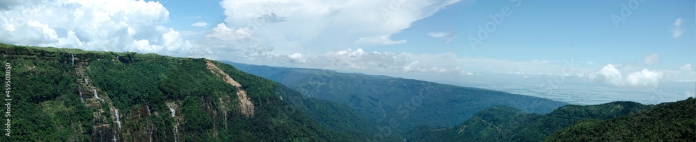Panorama view of a landscape, mountains, low lands, waterfalls, and blue cloudy sky Panorama view of a landscape, mountains, low lands, waterfalls, and blue cloudy sky