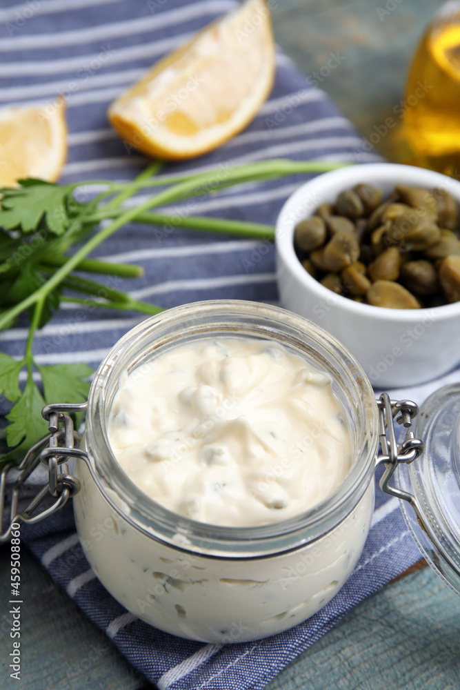 Tasty tartar sauce in glass jar and ingredients on light blue wooden table Tasty tartar sauce in glass jar and ingredients on light blue wooden table