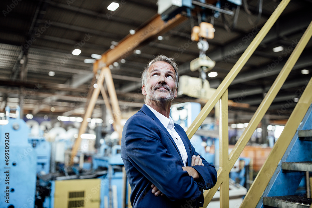 Thoughtful male professional standing with arms crossed in metal industry Thoughtful male professional standing with arms crossed in metal industry
