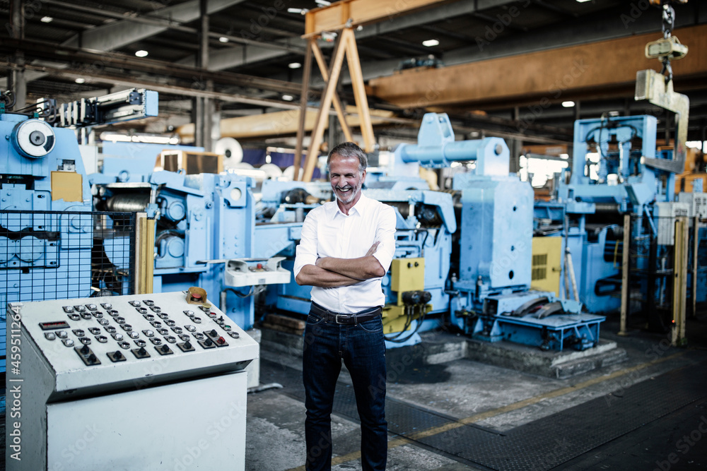 Cheerful businessman with arms crossed at manufacturing equipment Cheerful businessman with arms crossed at manufacturing equipment