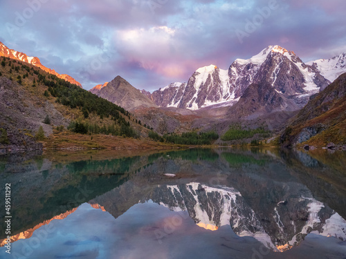 Sunset in magenta tones. Glacial lake high in the mountains. Atmospheric purple landscape with a lake in a high-altitude snowy mountain valley.