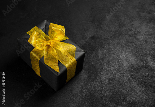 Gift box in black paper and with a gold bow on a black background.