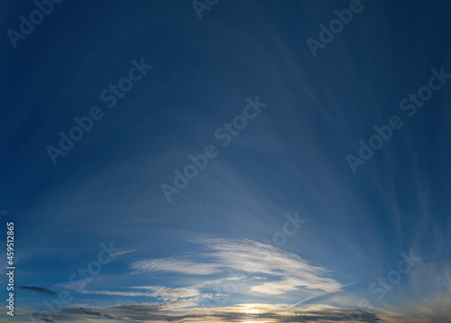 Panorama of the setting sun against a blue sky with openwork clouds
