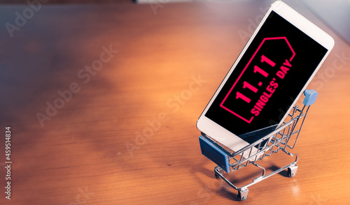 Smartphone with 11.11 message on screen inside a small shopping cart, singles day online shopping concept photo