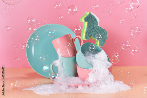 creative still life in bright colors with a sponge in the shape of a unicorn. The unicorn will say through the mountains of dirty dishes filled with foam for washing dishes surrounded by soap bubbles