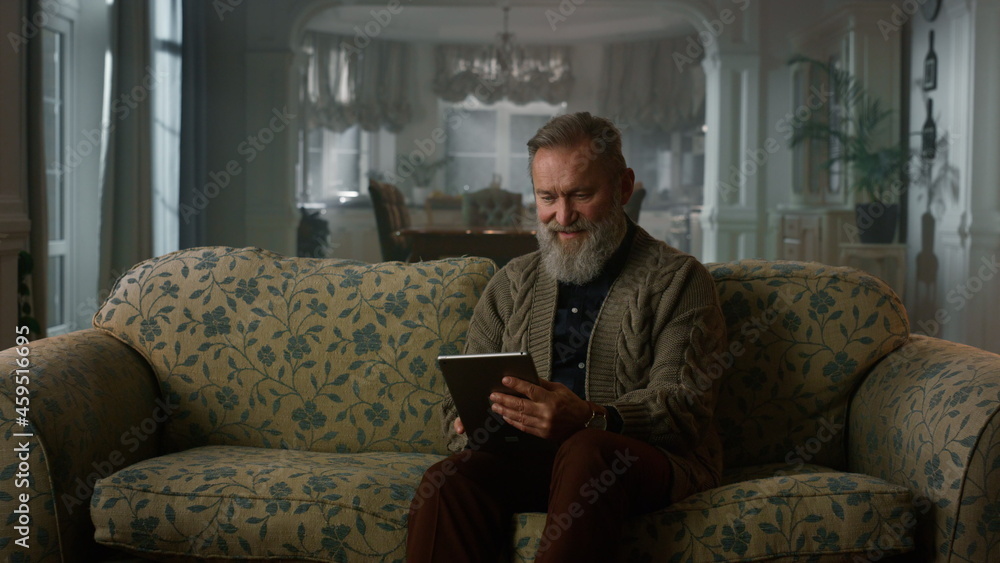 Calm senior man using tablet computer on sofa. Retired grandfather pad