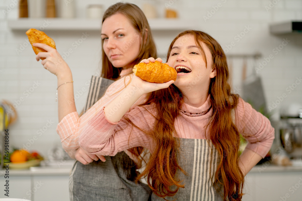 Caucasian daughter and her mother hold croissant and action with funny and happiness during cook together in home kitchen with healthy lifestyle.