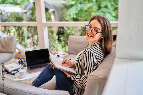 Portrait of happy smiling freelancer woman at home with notebook on the sofa