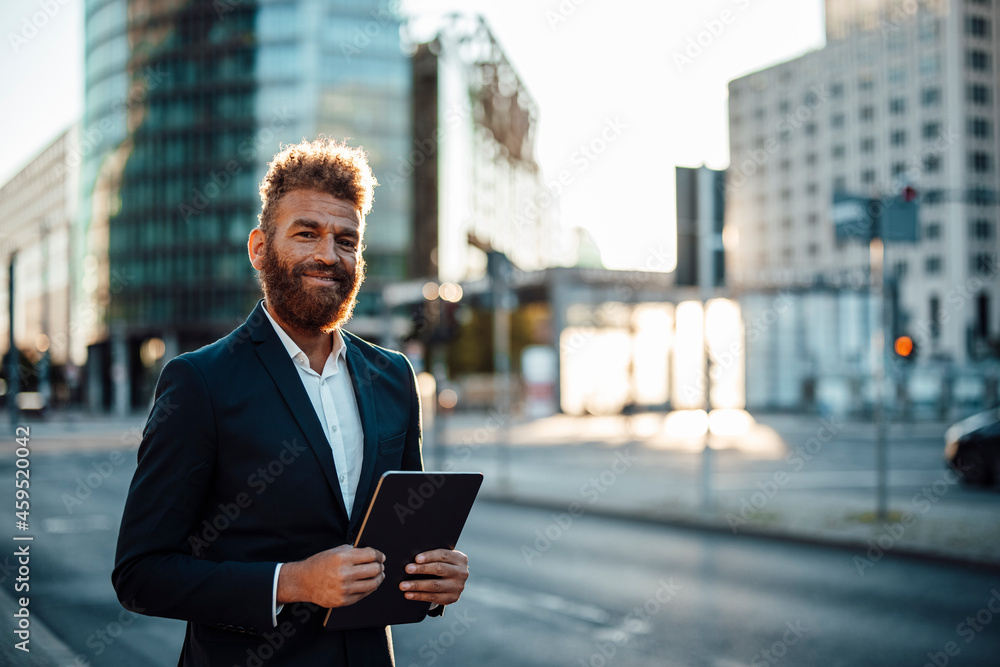 Smiling mature businessman with digital tablet standing on street