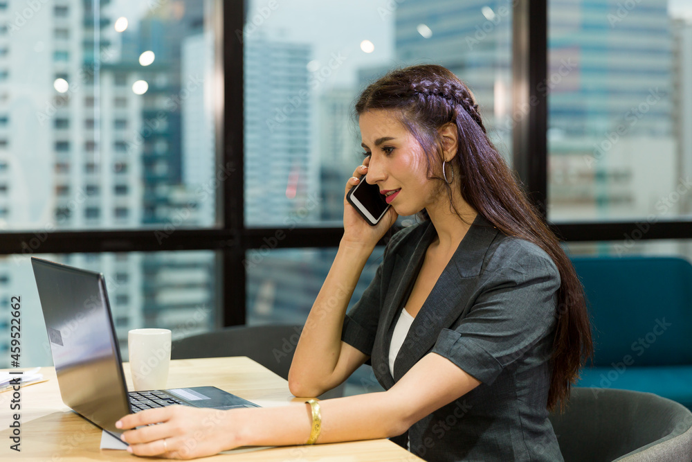 Business woman using mobile phone and working with laptop computer in the office. Beautiful woman working in the workplace Business woman using mobile phone and working with laptop computer in the office. Beautiful woman working in the workplace