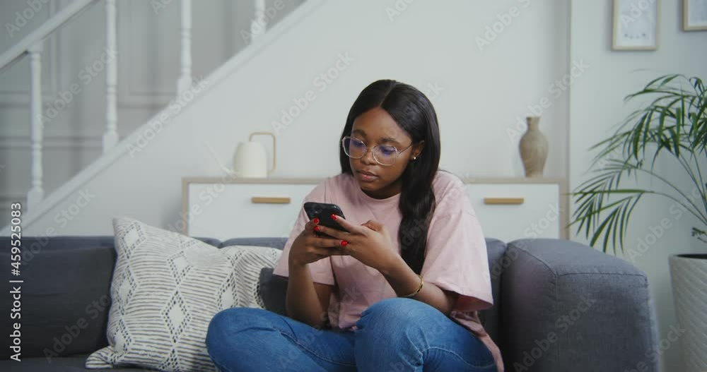 African american woman smiling when using the phone while sitting on the sofa African american woman smiling when using the phone while sitting on the sofa