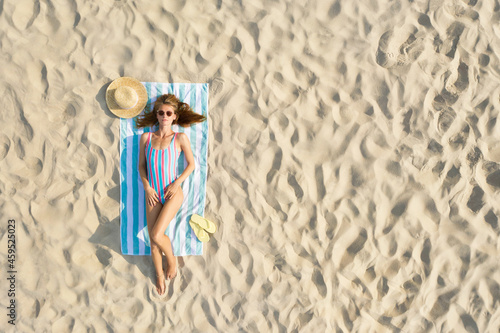 Woman sunbathing on beach towel at sandy coast, aerial view. Space for text photo