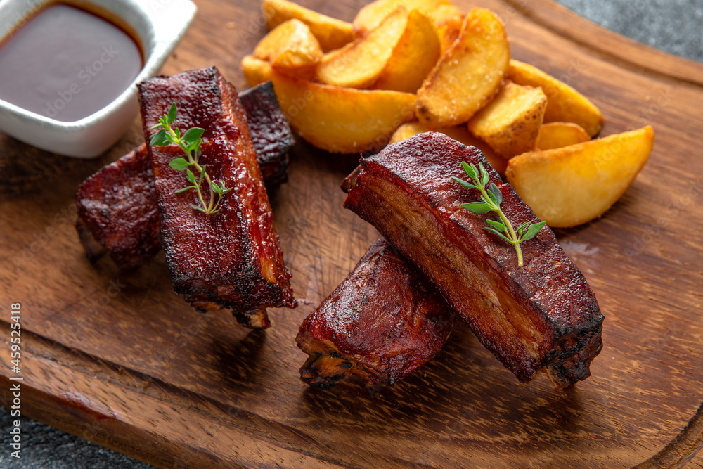 Grilled pork ribs plate with fried potatoes and barbecue sauce. Ready menu for the restaurant. Neutral gray blue textured background Grilled pork ribs plate with fried potatoes and barbecue sauce. Ready menu for the restaurant. Neutral gray blue textured background
