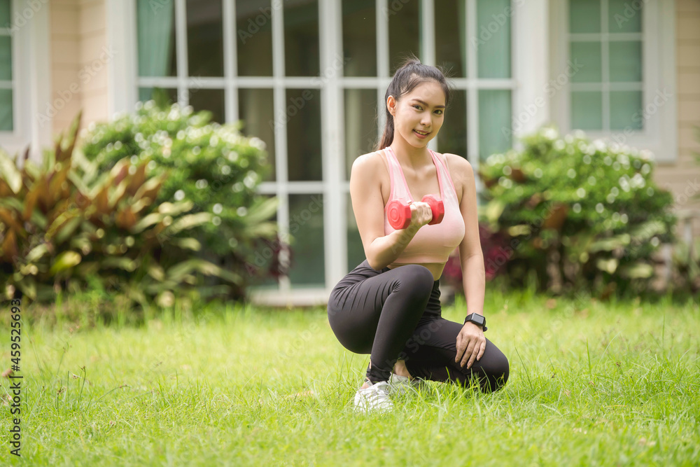 A sporty woman in sportswear exercises at the garden in front of her home A sporty woman in sportswear exercises at the garden in front of her home