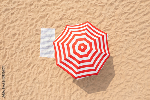 Striped beach umbrella near towel on sand, aerial view
