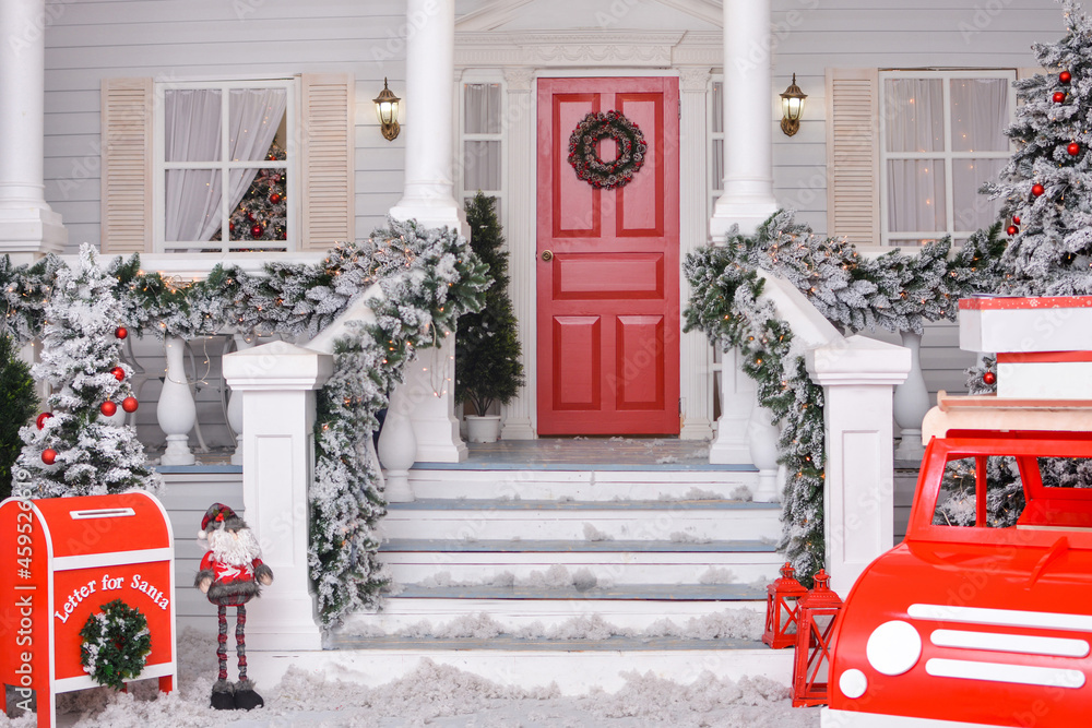 Fototapeta premium Christmas courtyard with Christmas porch, veranda, wreath, Christmas tree, red car, gnome, letterbox for Santa Claus, lanterns, garland. Merry Christmas and Happy New Year