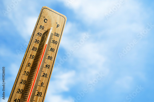 Wooden thermometer with red measuring liquid showing high temperature over 32 degrees Celsius on background of blue sky with clouds. Concept of heat wave, warm weather, global warming, climate change.