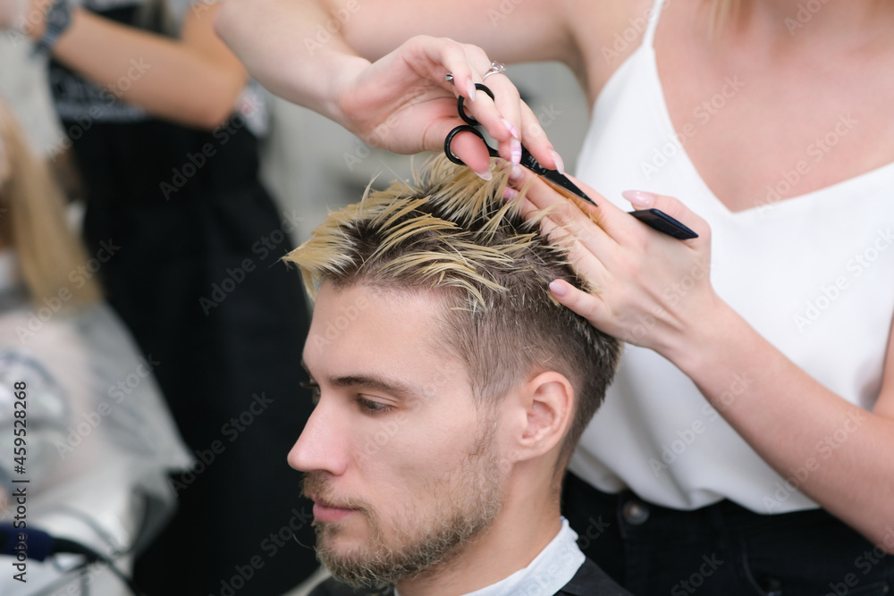 Fototapeta premium hairdresser cuts the hair of a young man with blond dyed hair with scissors in a beauty salon.