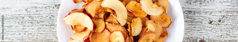 banner of A pile of dried apples in slices on a white plate on wooden background. Dried fruit chips. Healthy food