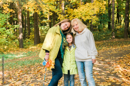 Portrait of three generations of happy beautiful woman looking at camera, hugging and smiling in autumn nature. © satura_