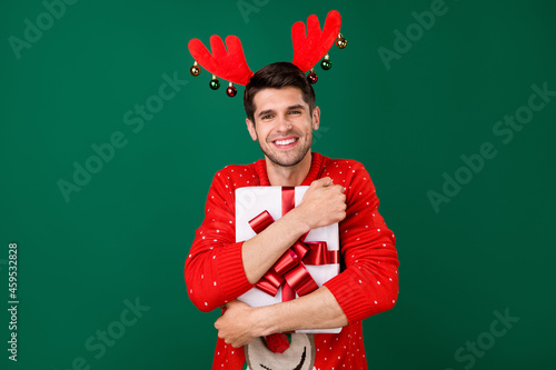 Photo portrait man in red knitted pullover embracing gift box on christmas smiling isolated green color background