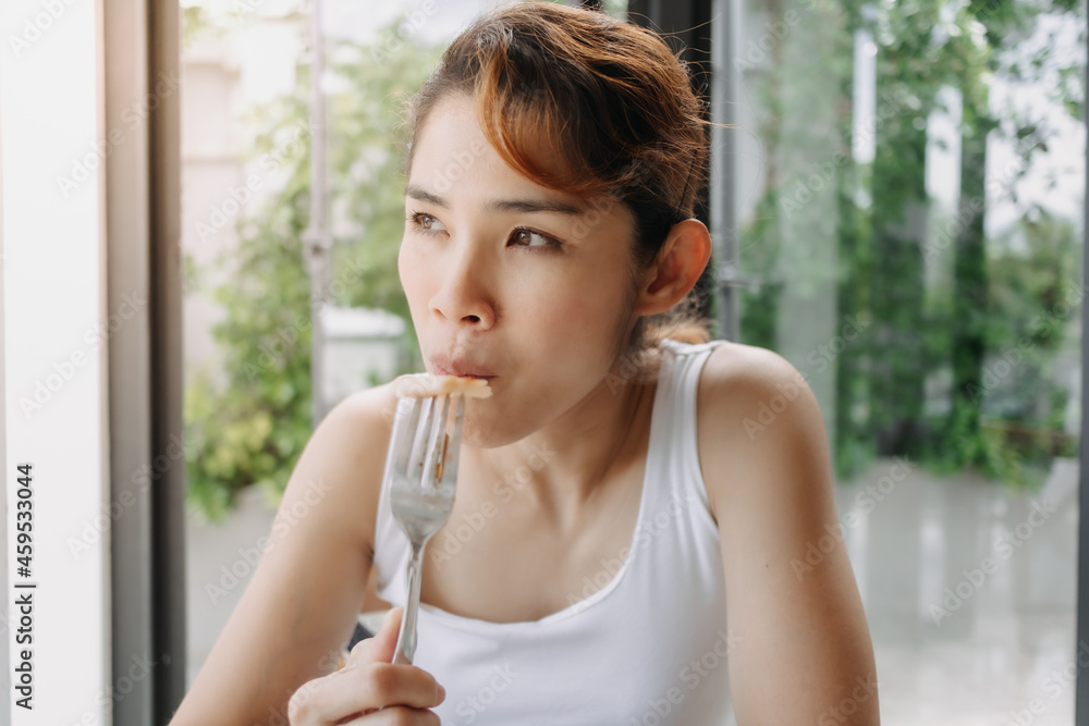 Asian woman in white tank top is having breakfast with fork.