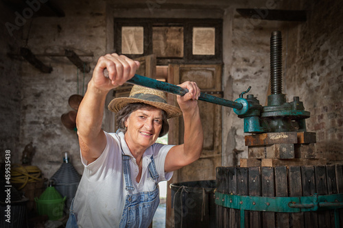 Bild auf Leinwand Grape harvest: Old woman smiling winemaker  working on a traditional winepress for the must pressing