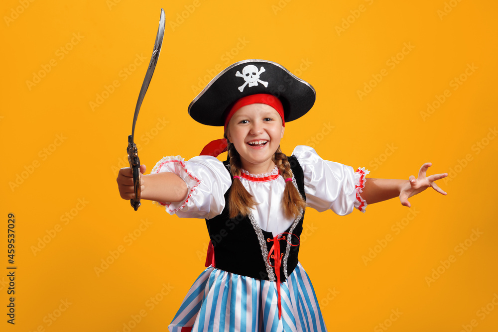 Naklejka premium Halloween celebration. Cheerful girl in a carnival costume of a pirate in the studio on a colored yellow background.