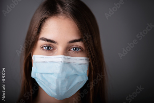 Close-up studio shot of young woman wearing face mask while standing at isolated background