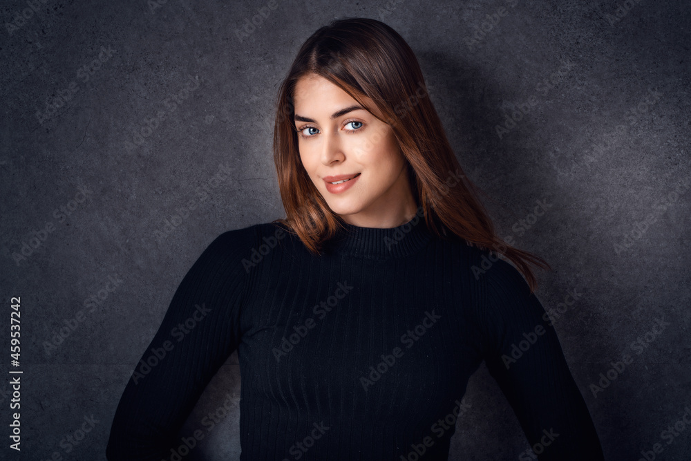 Attractive young woman studio portrait while standing at isolated dark background Attractive young woman studio portrait while standing at isolated dark background