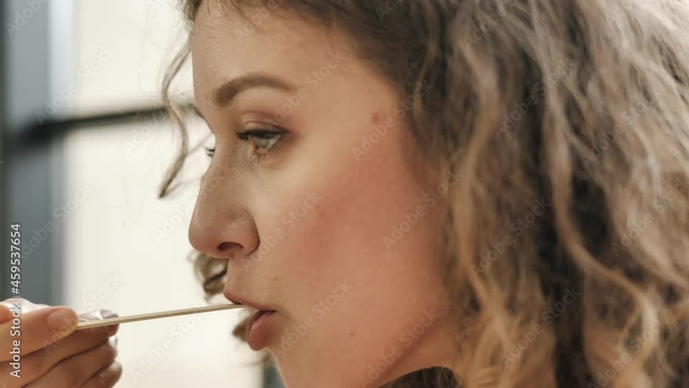 Curly haired young woman with light makeup licks lips eating dish with brown wooden fork and chews up food slowly extreme closeup Curly haired young woman with light makeup licks lips eating dish with brown wooden fork and chews up food slowly extreme closeup